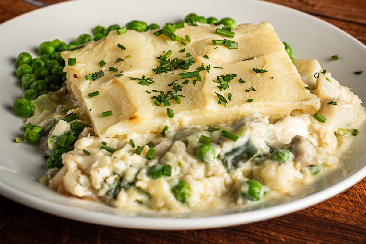 Close view of fish pie showing the mashed potato topping over a creamy white fish filling with peas and greens.